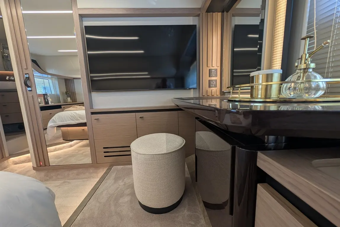 Modern bedroom interior featuring a wall-mounted TV, elegant furnishings, a round stool, and ambient lighting.